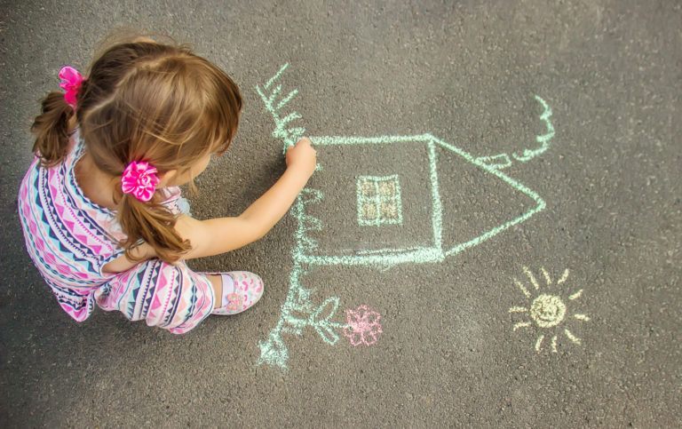 The child draws the house with chalk on the asphalt. Selective focus.